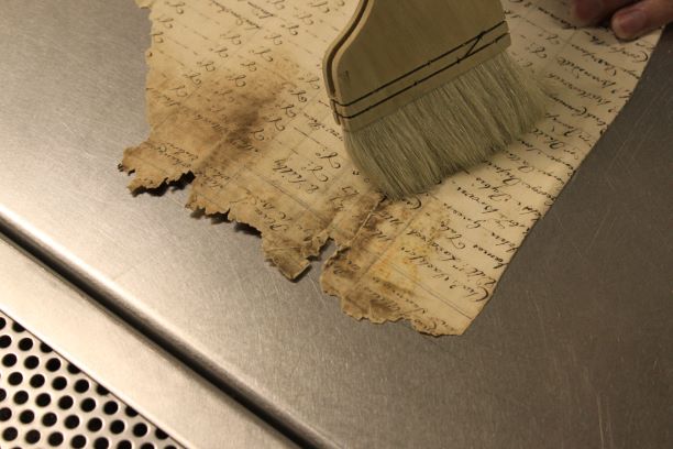 A colour photo showing a damaged document being cleaned with a large brush