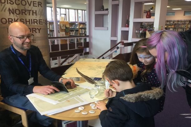 A colour photo showing a member of the Archives team sat at a table doing an activity with a family