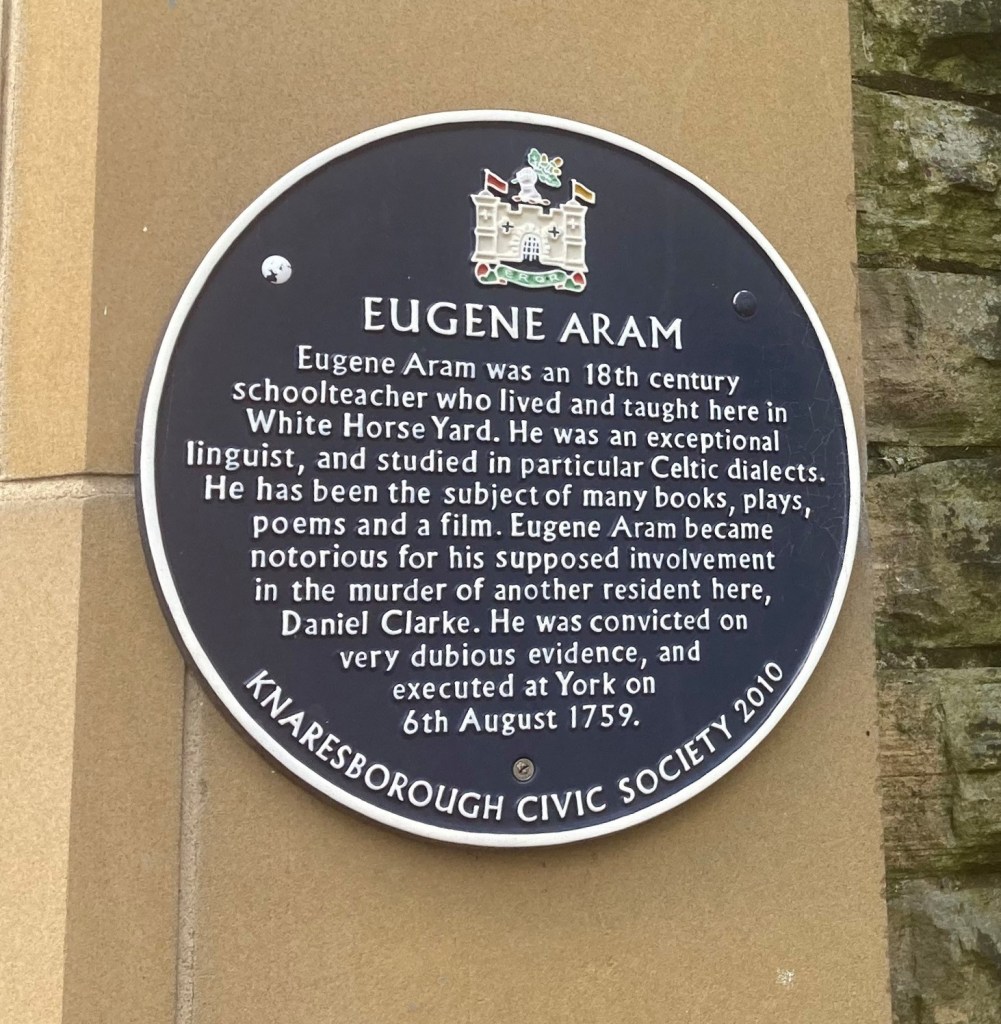 A blue plaque by Knaresborough Civic Society, dedicated to Eugene Aram in White Horse Yard. It reads:
Eugene Aram was an 18th century school teacher who lived and taught here in White Horse Yard. He was an exceptional linguist, and studied in particular Celtic dialects. He has been the subject of many books, plays, poems and a film. Eugene Aram became notorious for his supposed involvement in the murder of Daniel Clarke. He was convicted on very dubious evidence, and executed at York on 6th August 1759.